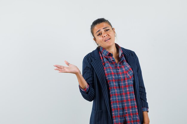 Lady spreading palm aside in shirt, jacket and looking confused , front view.