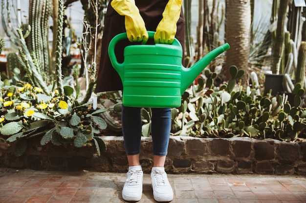 手注ぐ鍋で植物の近くの温室に立っている女性。