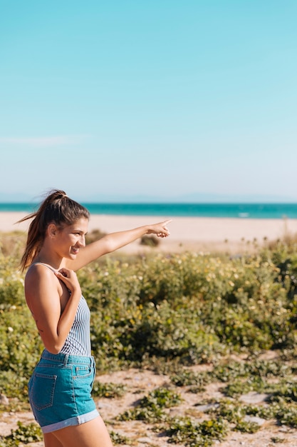 Free photo lady standing at seashore and showing hand forward