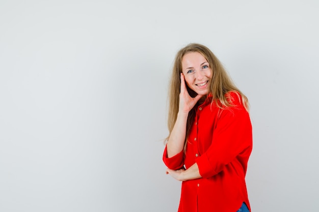 Lady standing in thinking pose in red shirt and looking cheerful.