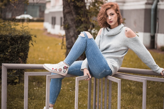 Lady in street wear sitting and putting leg on rail