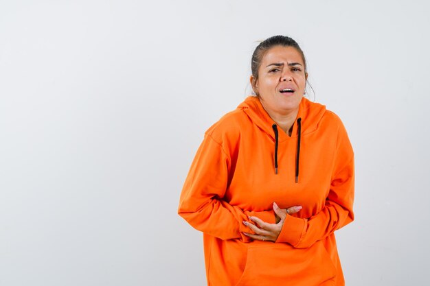 Lady suffering from stomach pain in orange hoodie and looking unwell