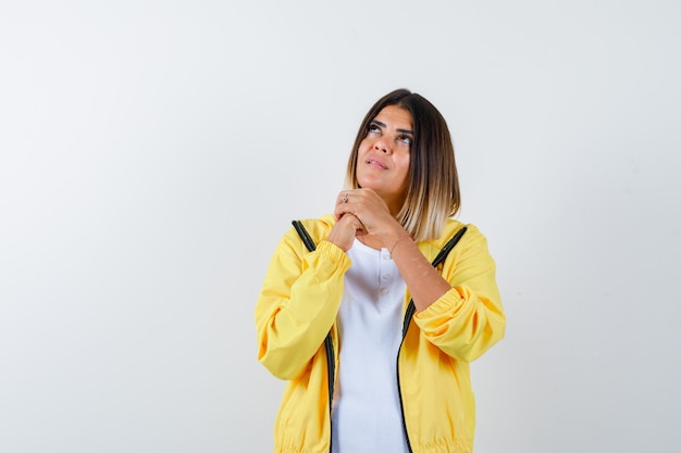 Lady in t-shirt, jacket clasping hands in praying gesture and looking hopeful , front view.