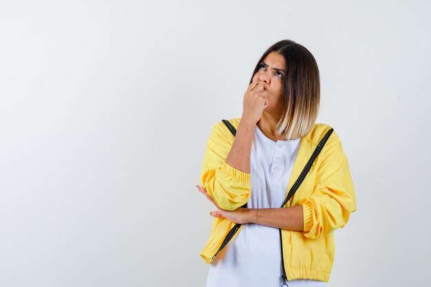 Lady in t-shirt, jacket keeping hand on chin and looking thoughtful , front view.