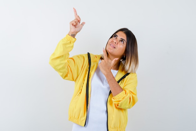 Lady in t-shirt, jacket pointing up and looking merry , front view.