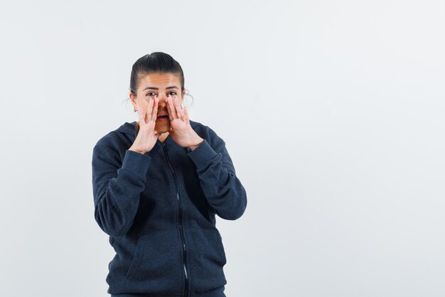 Lady telling secret with hands near mouth in hoodie front view.