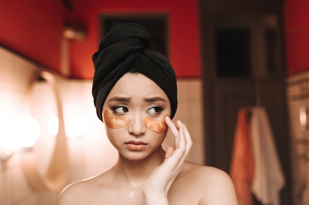 Lady in towel puts on patches to moisturize skin under eyes