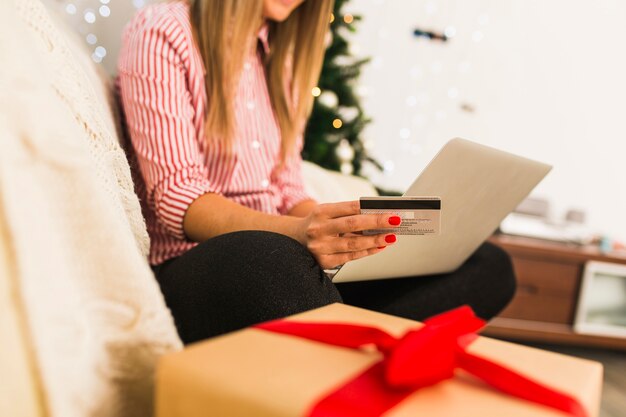 Lady using laptop and holding credit card near gift box