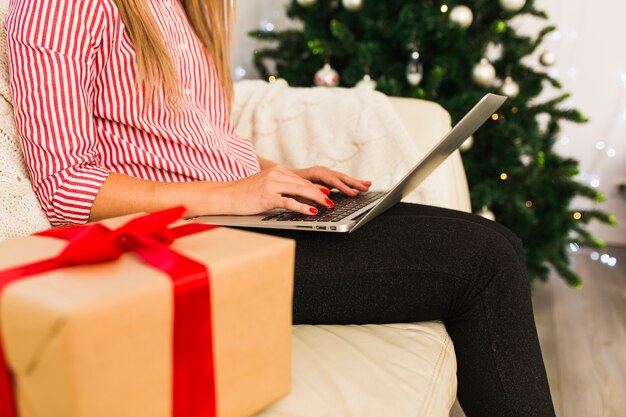 선물 상자와 크리스마스 트리 근처 노트북을 사용하는 여자