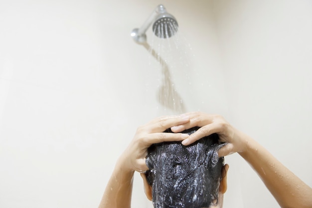 Леди, пользуясь шампунем, моет / моет волосы в ванной комнате с брызгами воды