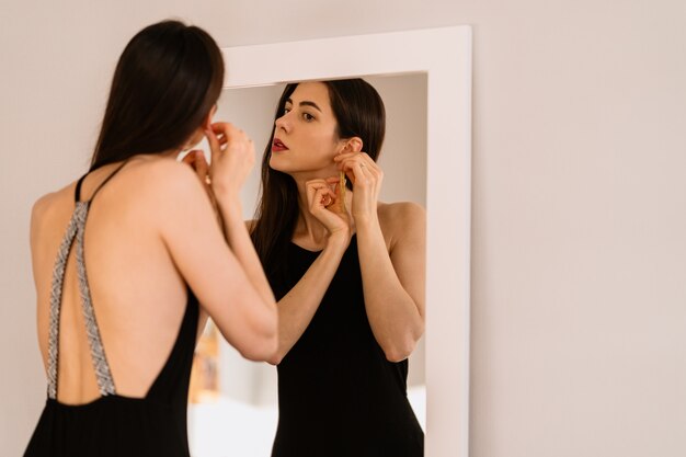 女性は鏡を見る美しい黒のドレスを着ています。
