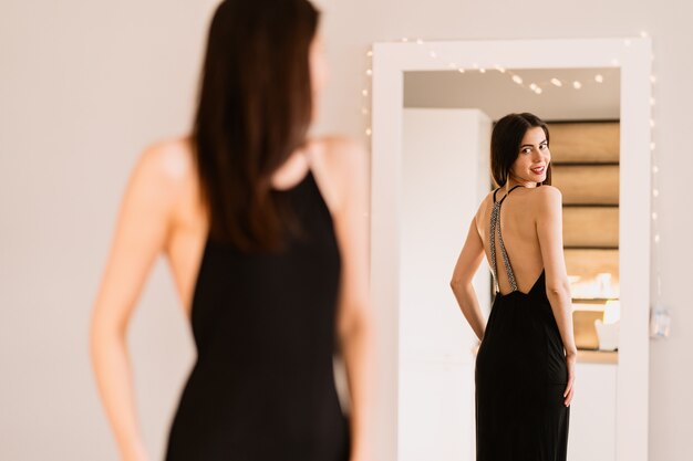 레이디는 거울을보고 아름다운 검은 드레스를 입는다.
