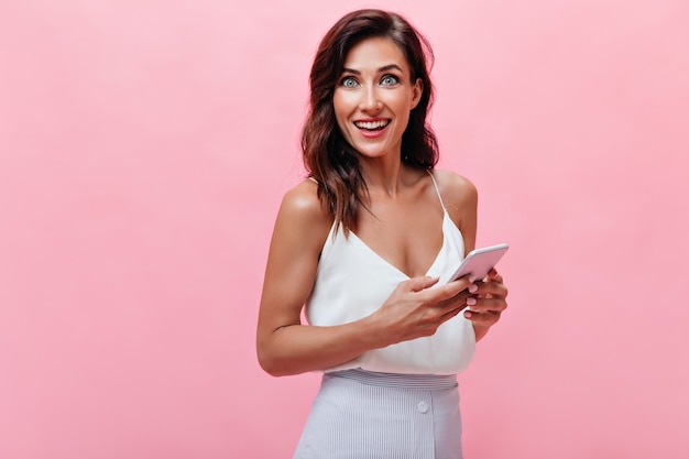 Lady in white top stares into camera in amazement and holds phone