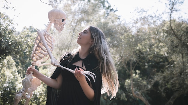 Lady in witch costume holding gloomy skeleton 