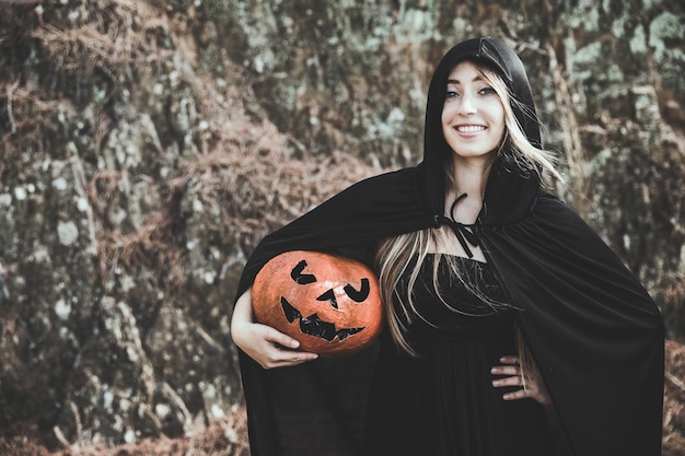 Lady in witch suit with hood on head holding pumpkin