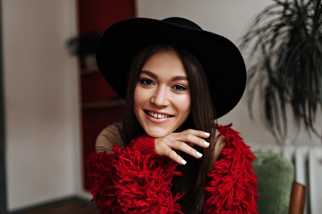 Lady with dark hair and brown eyes with sweet smile looks into camera Portrait of woman wearing red wool jacket and widebrimmed hat