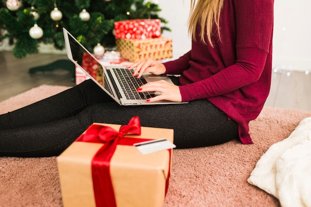 Lady with laptop near credit card, gift box and Christmas tree