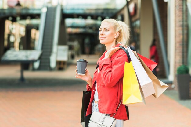 買い物用のパケットとドリンクのカップを持つ女性