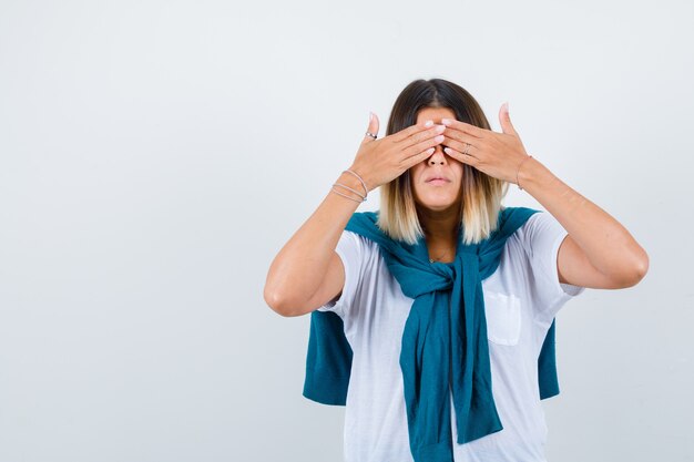 Lady with tied sweater keeping hands on eyes in white t-shirt and looking scared. front view.