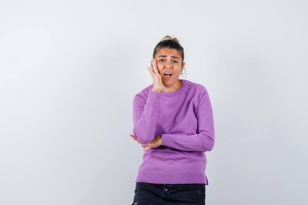 Lady in wool blouse keeping hand on cheek and looking surprised 