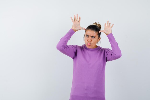 Lady in wool blouse keeping hands over head as ears and looking funny 