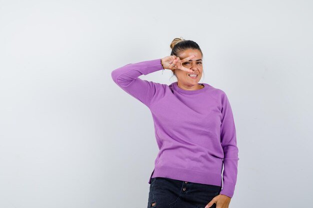 Lady in wool blouse showing V-sign on eye and looking merry 