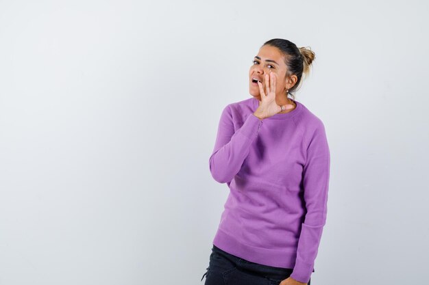 Lady in wool blouse telling secret behind hand and looking curious 