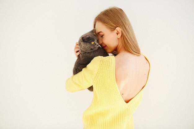 Lady in yellow dress with open back holds grey cat on her shoulder