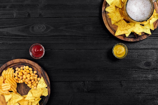 Lager beer and snacks on black wooden table. Nuts, chips. Top view with copyspace. Still life. Flat lay