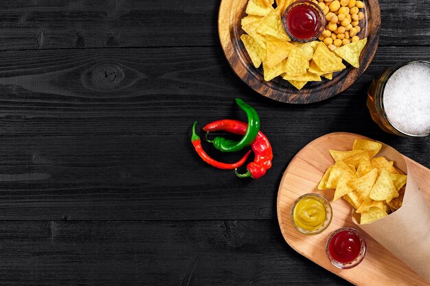 Lager beer and snacks on black wooden table. Nuts, chips. Top view with copyspace