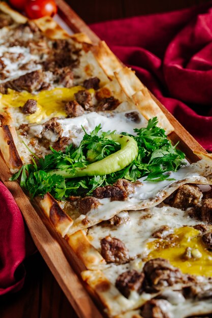 Lahmacun slices with meat and oily stuff and herbs on it on a red tablecloth.