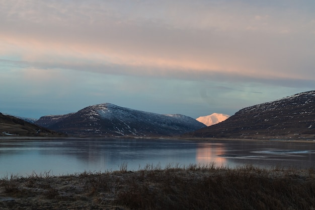 アイスランドの日没時に水に反射して雪に覆われた丘に囲まれた湖