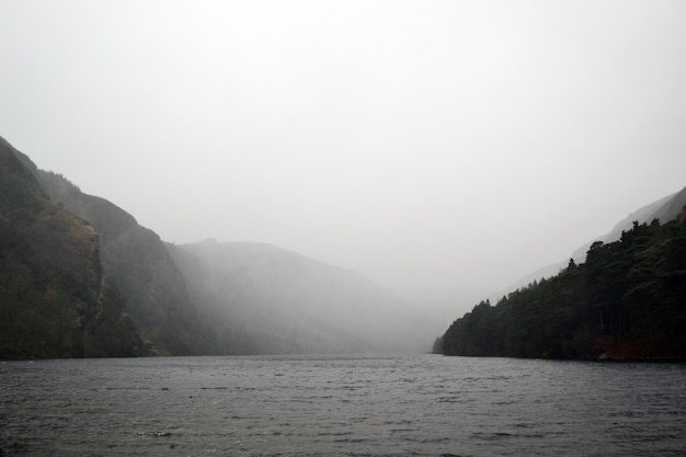 Lago circondato da colline sotto il cielo grigio nebbioso