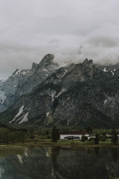 Lake surrounded by trees and rocky mountains covered in the fog under a cloudy sky