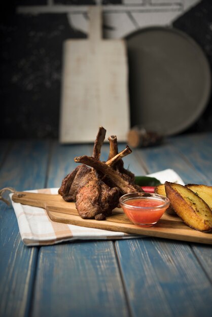 Lamb chops on wooden board with potatoes and sauce