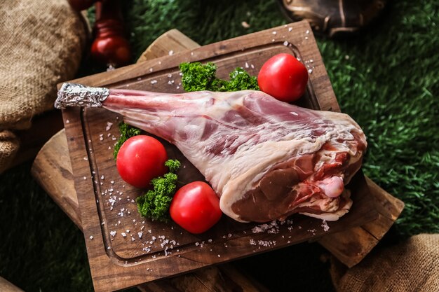 Lamb leg on the wooden board prepared for cook tomato broccoli salt top view