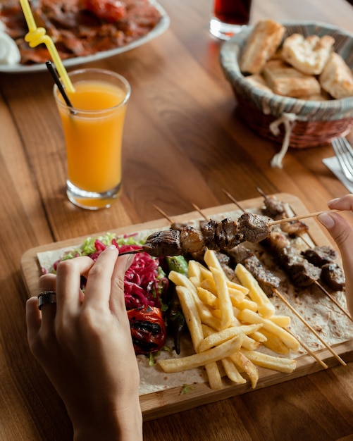 Kebab di agnello su spiedini di bambù servito con patatine fritte, cavolo sottaceto, insalata