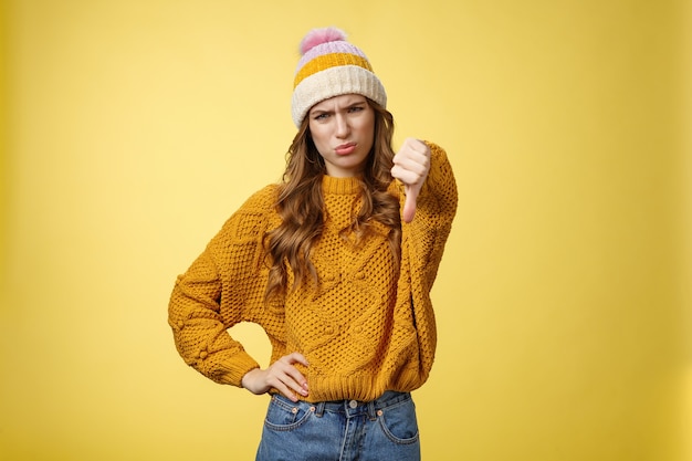 Lame dislike unfollow. Portrait disappointed displeased picky young judgemental woman show thumb-down cringing grimacing unsatisfied expressing disapproval antipathy, yellow background