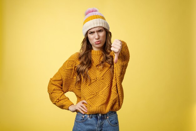 Lame dislike unfollow. Portrait disappointed displeased picky young judgemental woman show thumb-down cringing grimacing unsatisfied expressing disapproval antipathy, yellow background