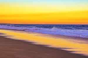 Free photo landscape of a beach surrounded by sea waves during an orange sunset in the evening