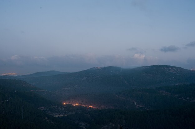 저녁 동안 흐린 하늘 아래 숲과 빛으로 덮여 언덕의 풍경