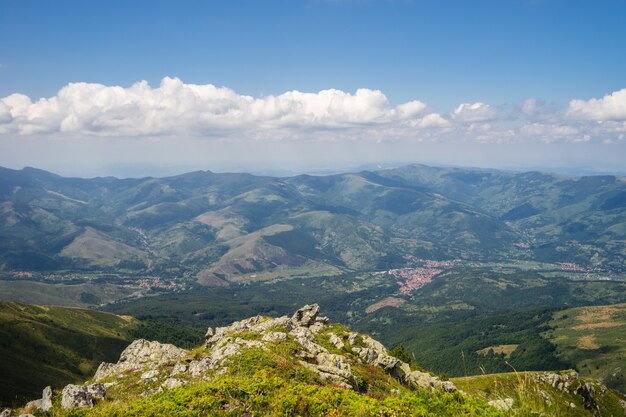 Landscape of hills covered in greenery with rocky mountains under a cloudy sky on the