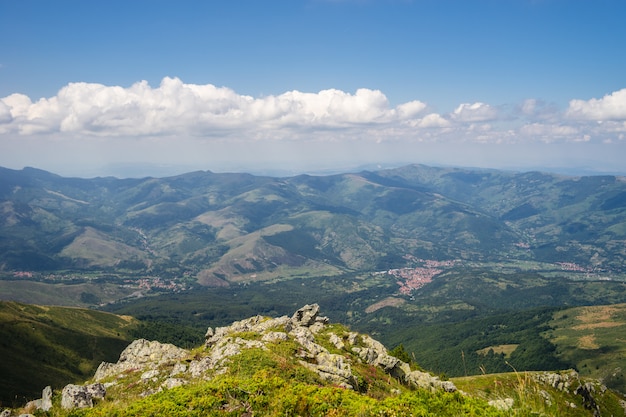 Landscape of hills covered in greenery with rocky mountains under a cloudy sky on the