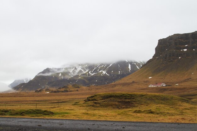 アイスランドの曇り空の下で雪と草で覆われた丘の風景