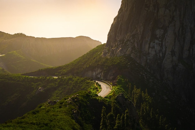 Landscape of mountains covered in greenery with roads on them under a cloudy sky during sunset
