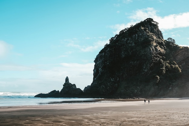 Landscape of the Piha beach and high rocks with the people walking around it under a blue sky
