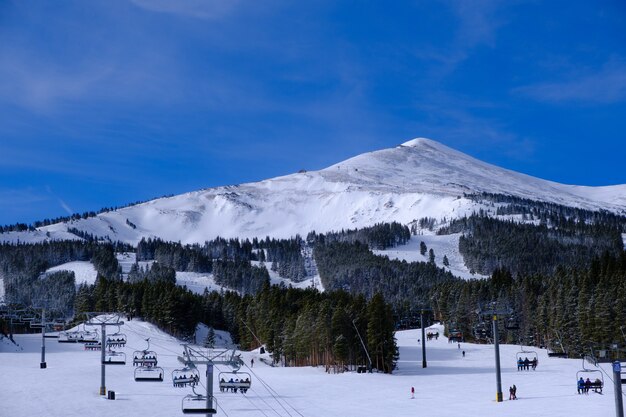 青い空の下で雪に覆われた丘や森に囲まれたロープウェイの風景