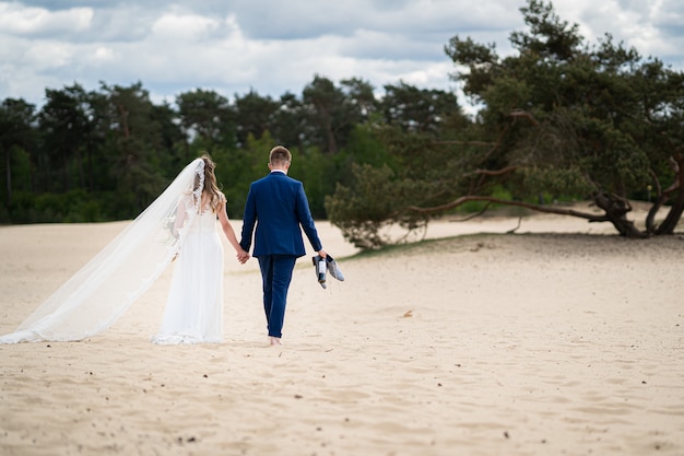 Landscape shot of a couple walking on sand on their wedding day