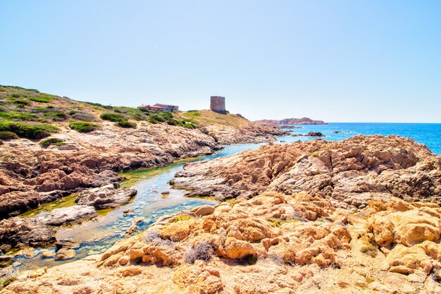 Landscape shot of rocky hills with castle building near the open sea with a clear sunny blue sky