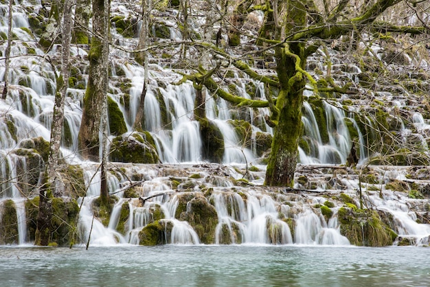 Landscape shot of a waterfall flowing from mossy cliffs into a lake